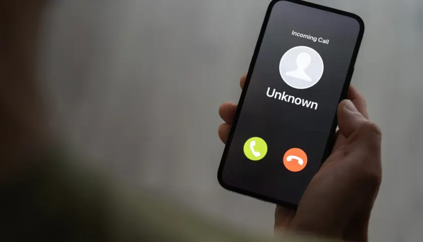Dłoń trzyma smartfon z ekranem blokady, na którym widnieje "Incoming Call" od nieznanego numeru. Uważaj na vishing!