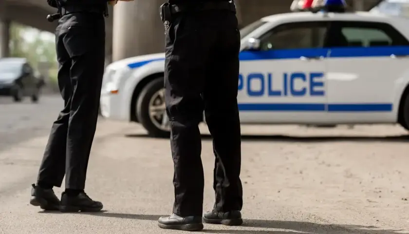 Policjanci w pełnym umundurowaniu stoją obok radiowozu. Ich wyposażenie jest gotowe do akcji.