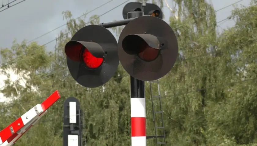 Czerwone światła na przejeździe kolejowo-drogowym ostrzegają przed nadjeżdżającym pociągiem. Zapora jest opuszczona.