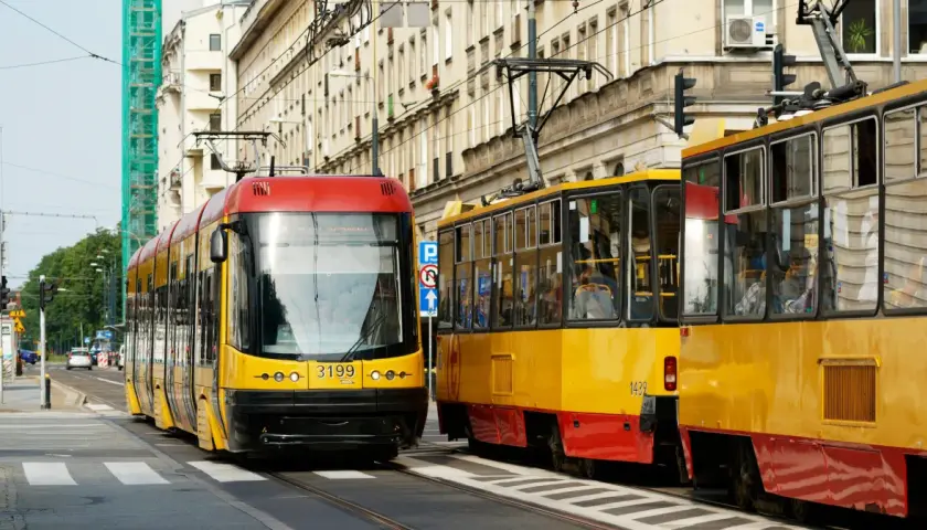 Dwa żółto-czerwone tramwaje stoją na ulicy, jeden z nich ma pierwszeństwo.