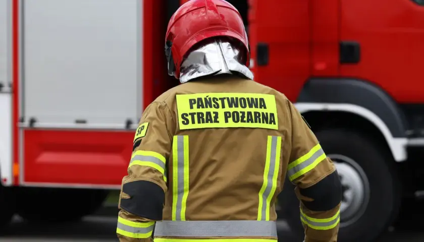 Strażak w hełmie i kurtce z napisem "Państwowa Straż Pożarna" gotowy do akcji. Alarm bombowy? Nie, to tylko ćwiczenia.