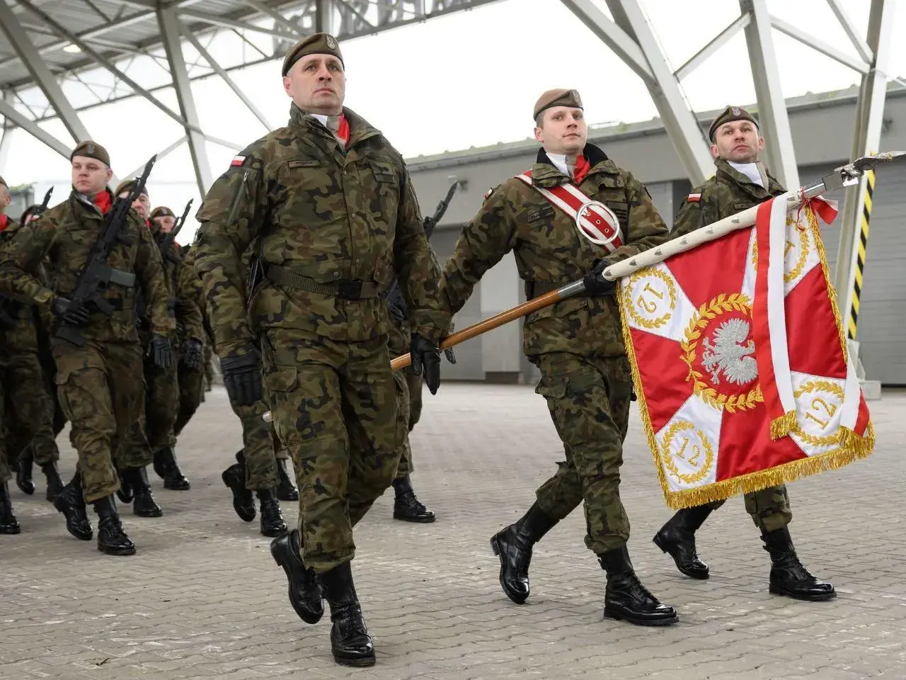 Żołnierze w mundurach maszerują z flagą. Uroczysta przysięga wojskowa w pełnym rynsztunku.