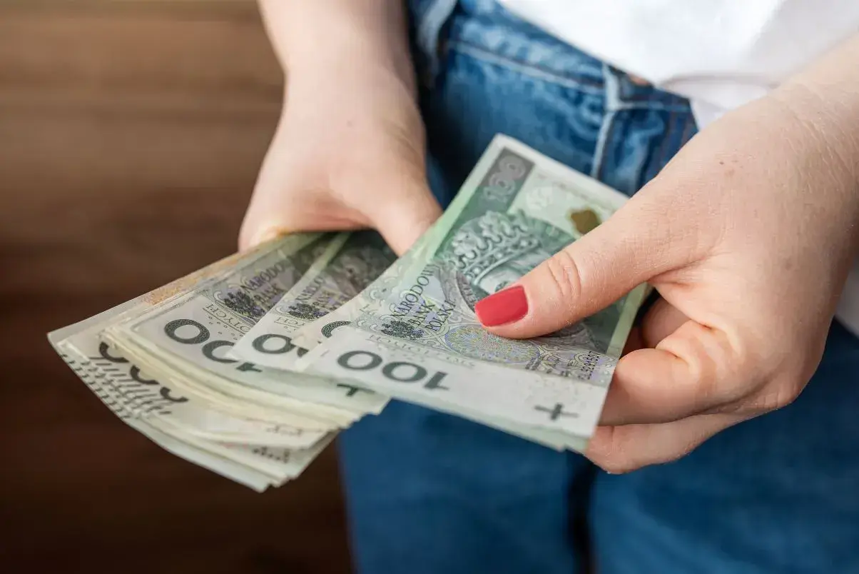 Dłonie trzymające stos banknotów 100 zł. Czy to przyszła kwota bazowa służba cywilna 2026?
