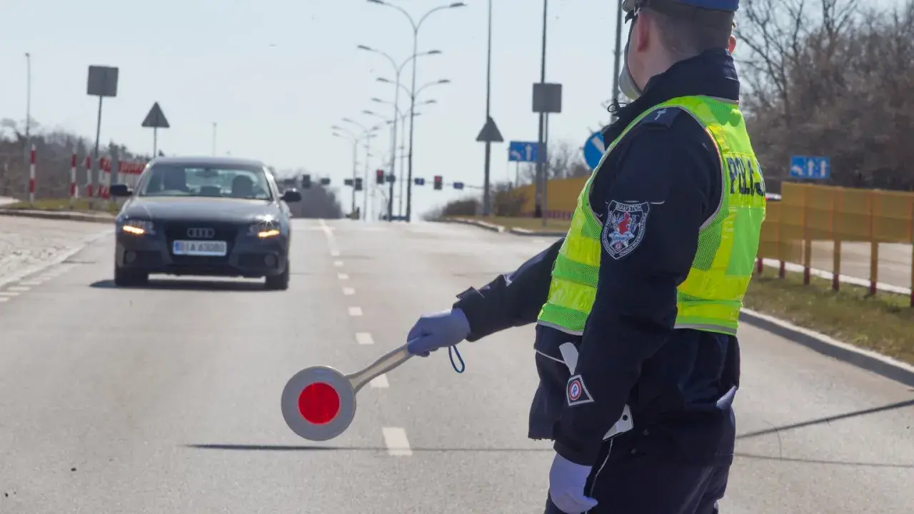 Policjant kieruje ruchem, egzekwując przepisy ruchu drogowego. Na drodze stoi samochód.