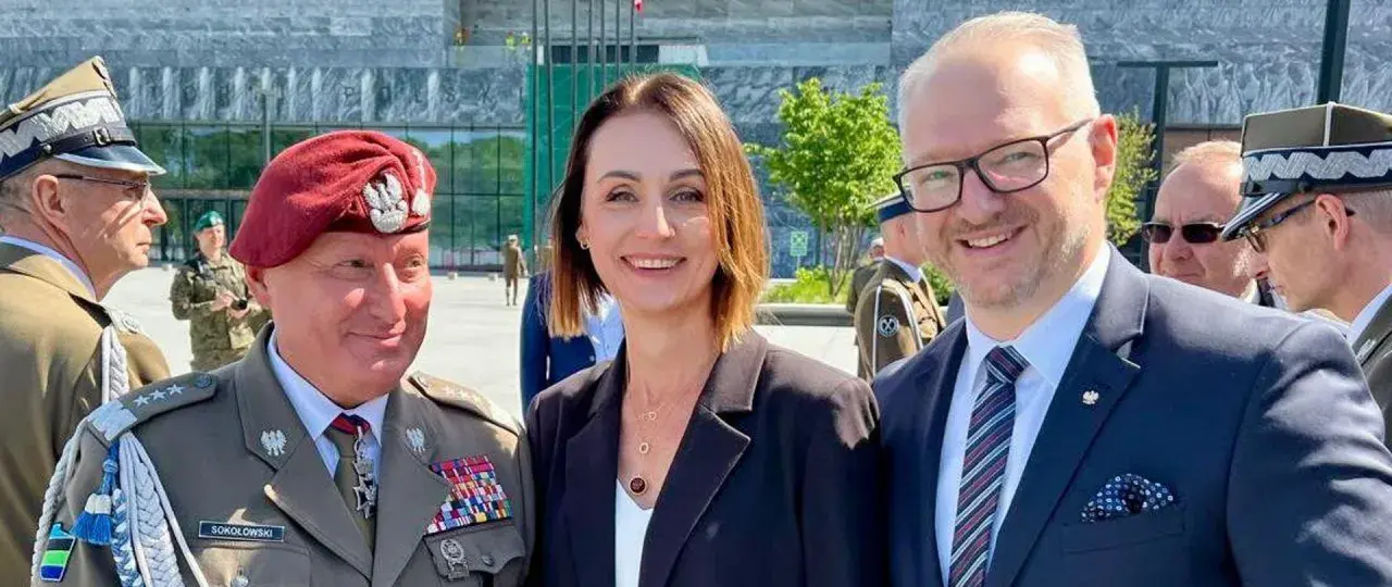 Dowódca generalny rodzajów sił zbrojnych w towarzystwie kobiety i mężczyzny w garniturze, na tle nowoczesnego budynku.