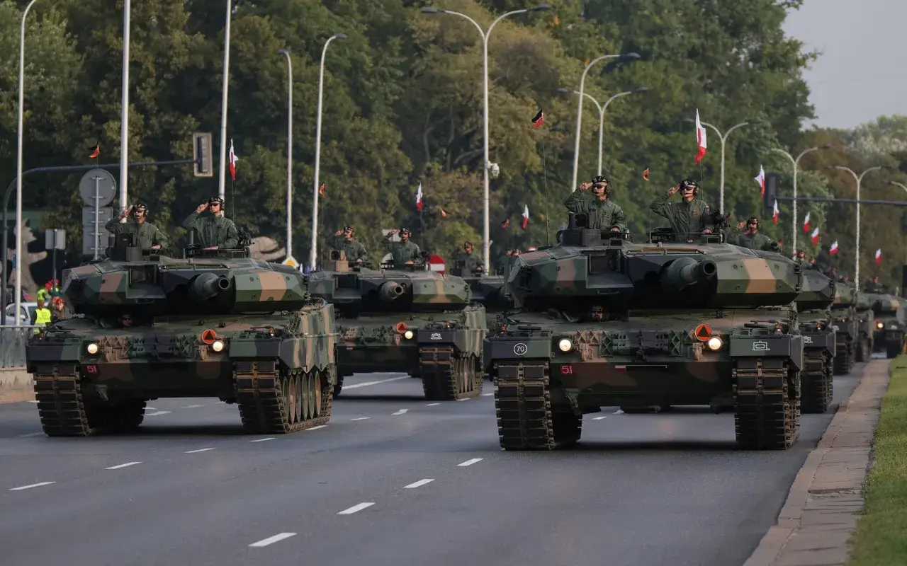 Parada wojskowa z nowoczesnym uzbrojeniem. Czołgi Leopard 2 maszerują ulicą, żołnierze pozdrawiają.