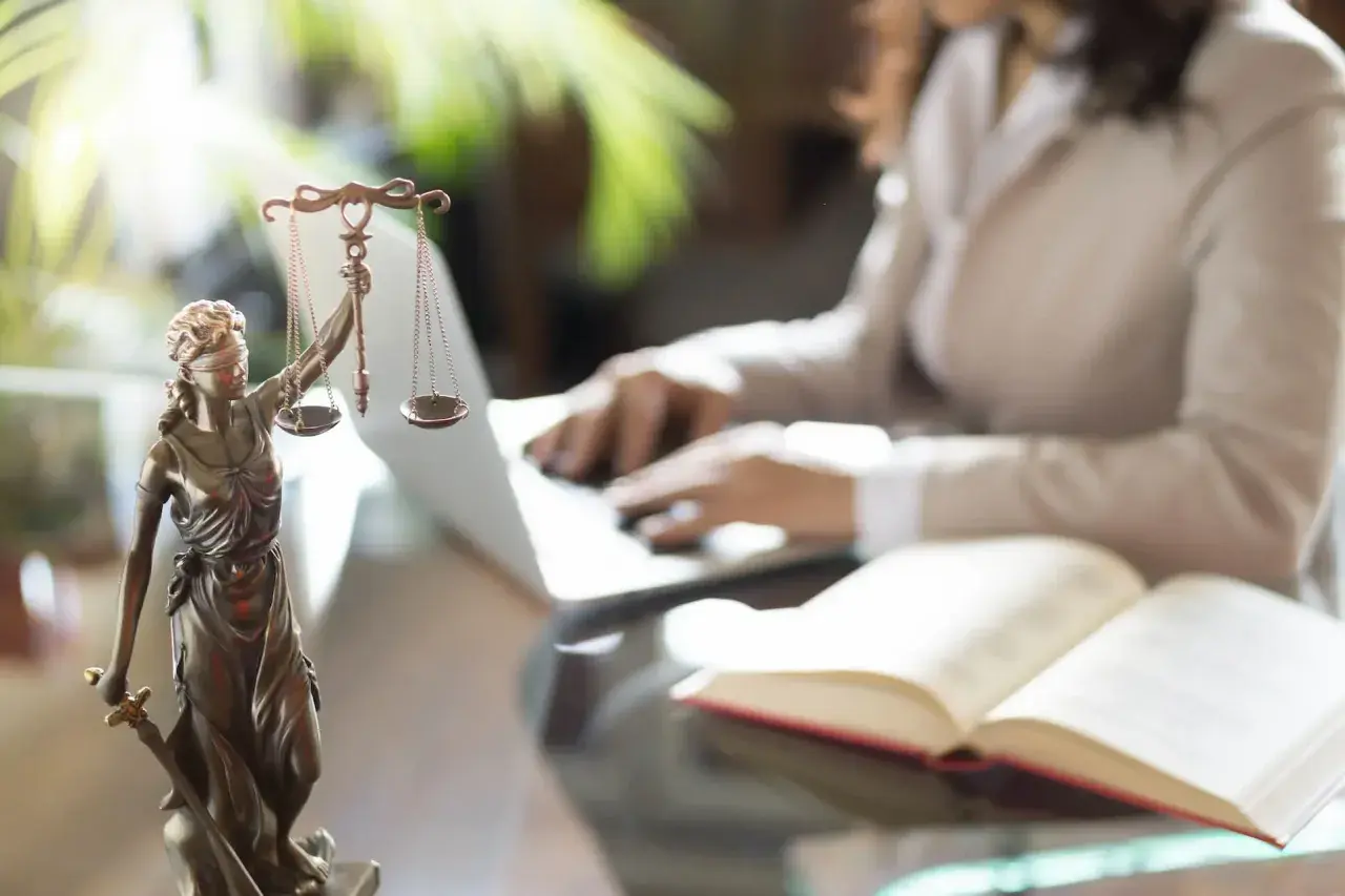 Figurka Temidy z wagą i mieczem, obok otwarta księga i osoba pracująca przy laptopie. Symbol sprawiedliwości i abolicji.