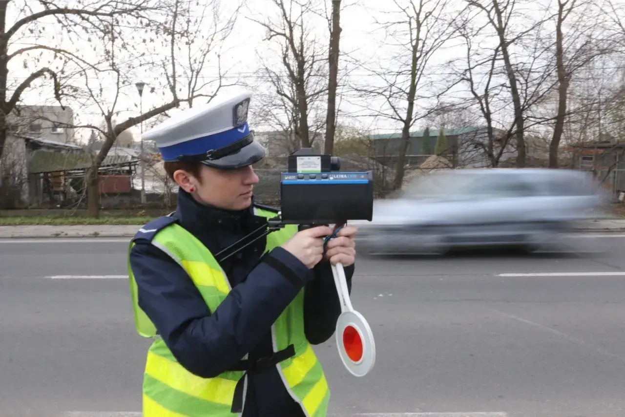 Policjantka w kamizelce odblaskowej mierzy prędkość przejeżdżającego samochodu radarem.
