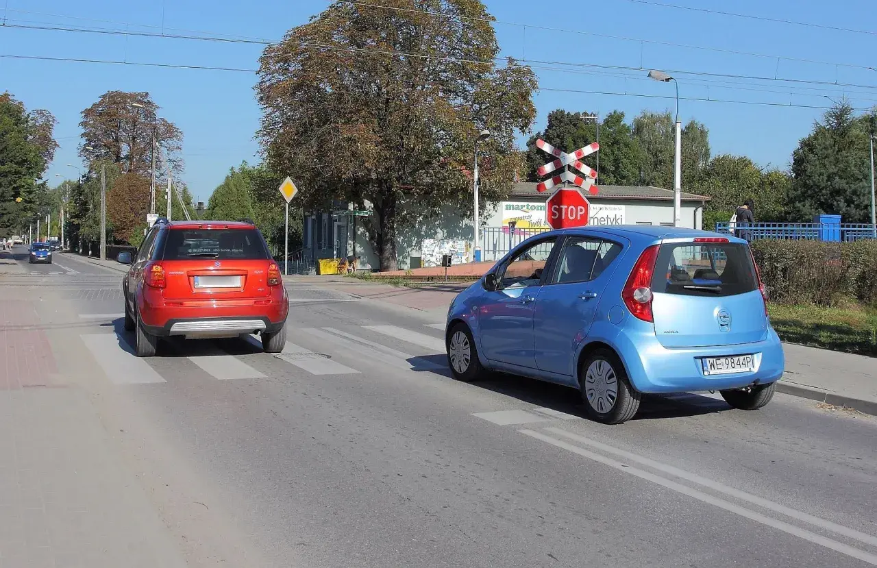 Czerwony i niebieski samochód na przejściu dla pieszych, czerwony czeka na wymijanie, niebieski już rusza.