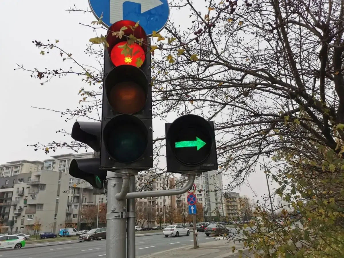 Sygnalizator S2 z czerwonym światłem na górze i zieloną strzałką w prawo. Za nim drzewa i budynki.