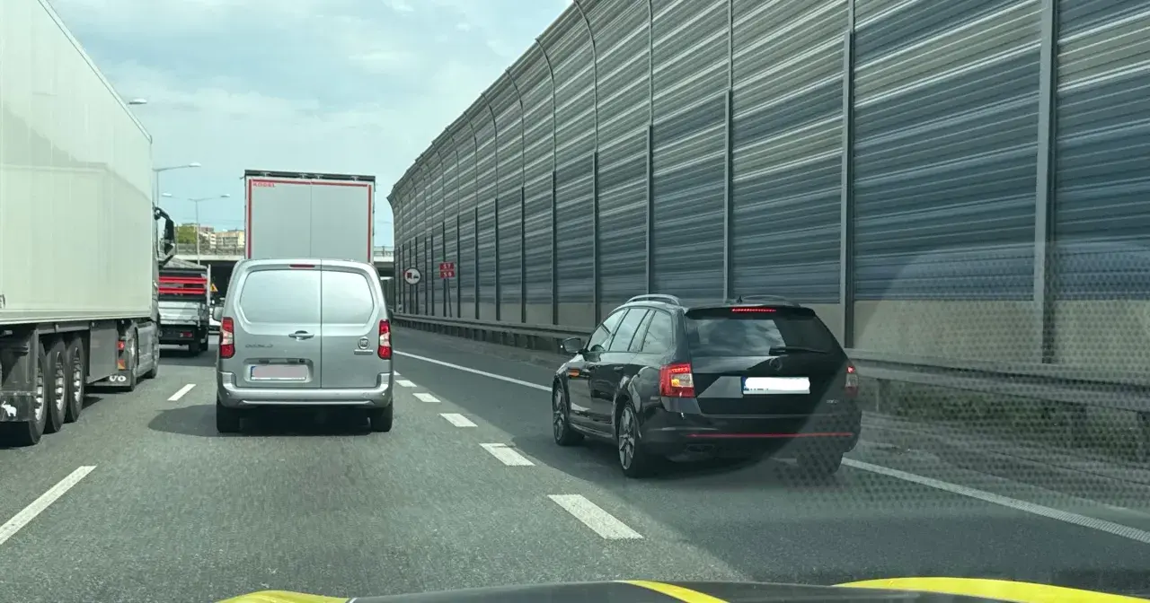 Kork na autostradzie, samochody i ciężarówki stoją w korku. Widać znak informujący o jeździe na suwak.