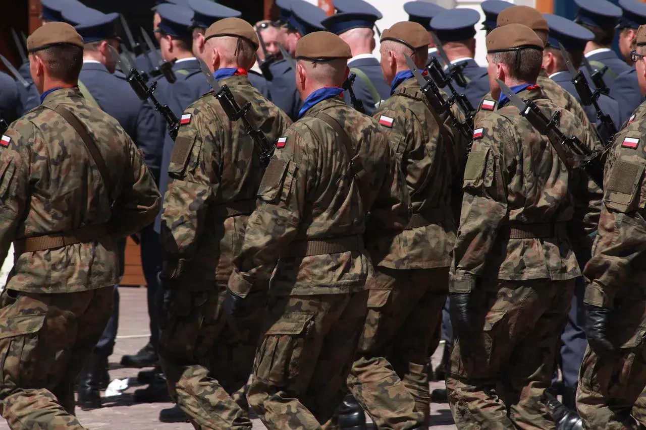 Żołnierze w mundurach polowych, z karabinami, maszerują w szyku. Widać polskie flagi na rękawach. To wyższy stopień podoficerski w marynarce wojennej.