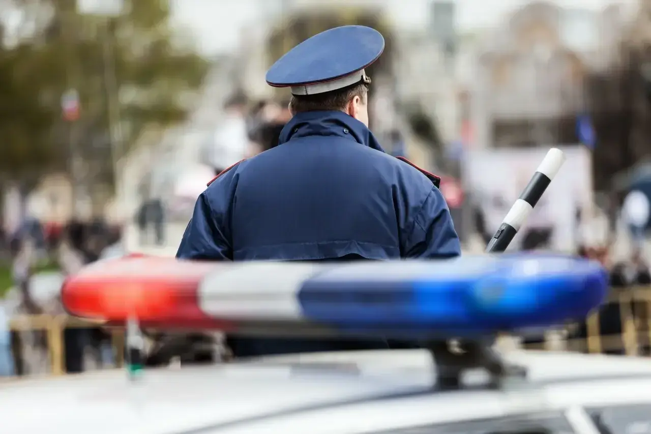 Policjant w mundurze stoi przy radiowozie. Zastanawiasz się, ile zarabia policja kryminalna?