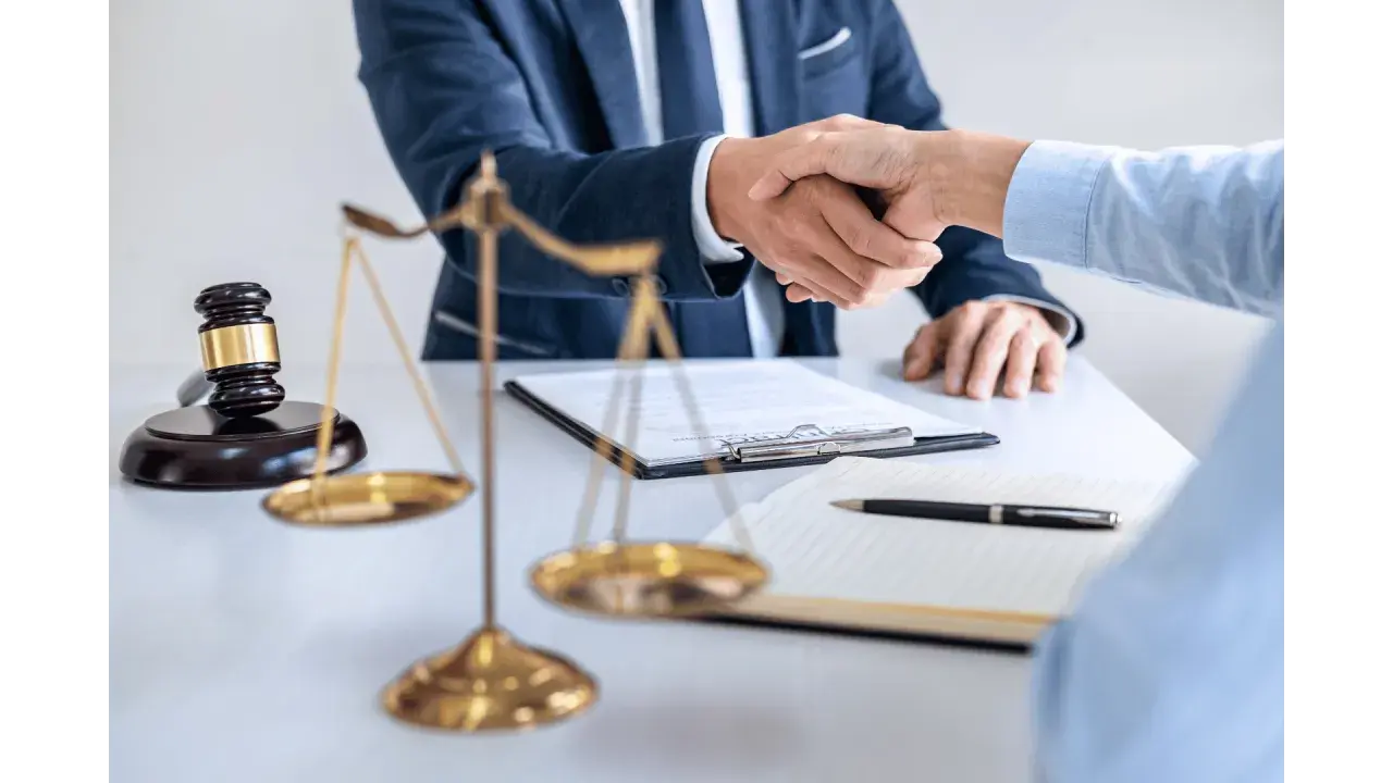 Uścisk dłoni prawników przy biurku z wagą sprawiedliwości i młotkiem. Sprawa 157 kk zakończona sukcesem.
