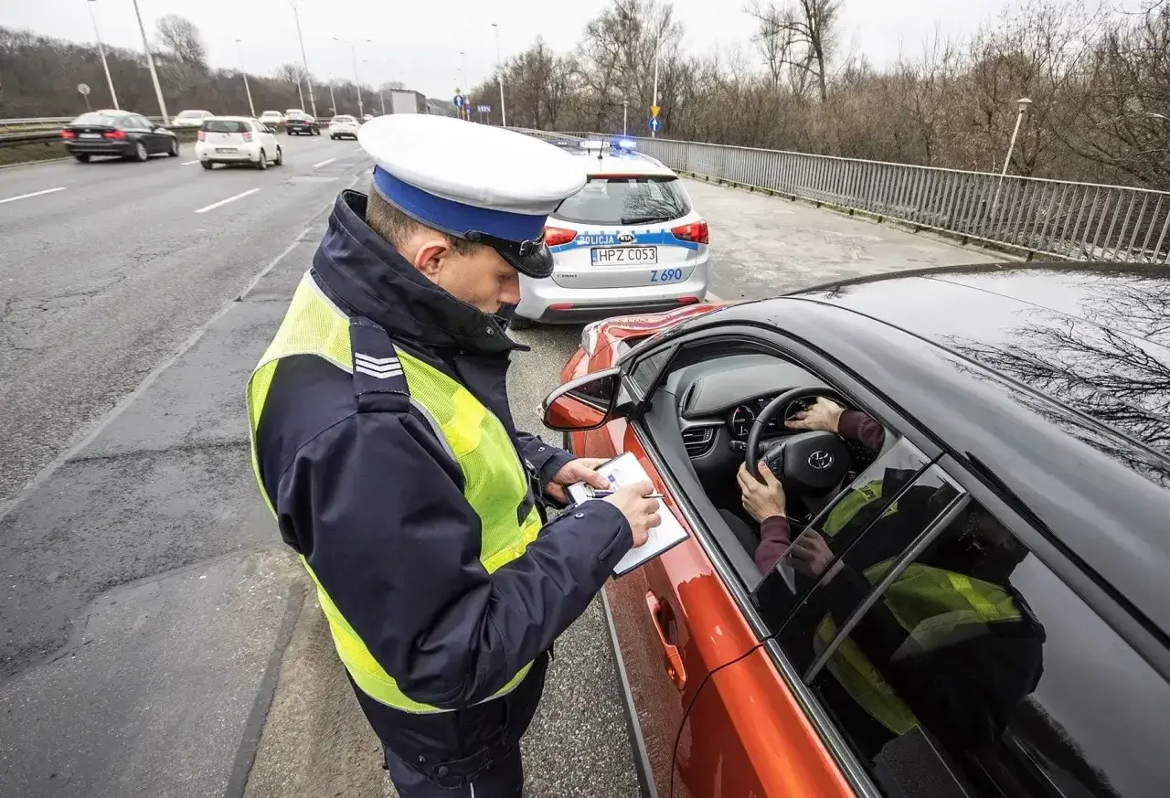 Policjant spisuje mandat, art. 97 kw. Kierowca w kamizelce odblaskowej zatrzymany do kontroli drogowej.