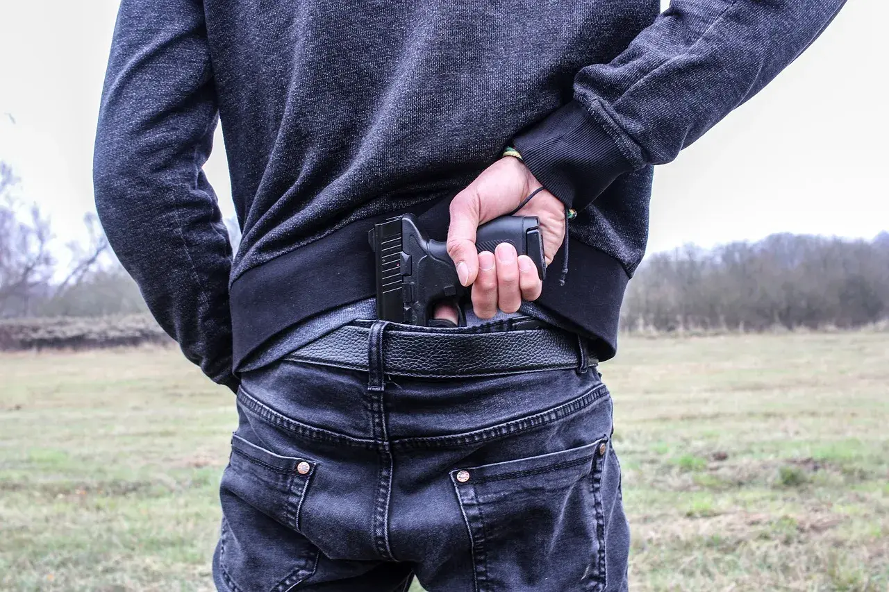 Mężczyzna chowa pistolet za pasem, gotowy do egzekwowania haraczu.