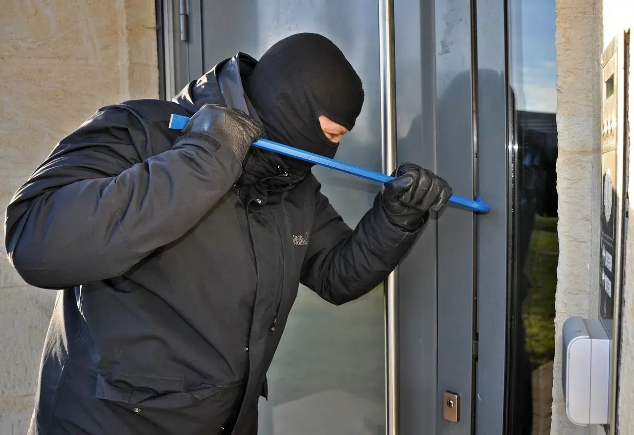 Złodziej w kominiarce i rękawiczkach próbuje wyważyć drzwi łomem. To może być próba włamania, zgodnie z art. 279 kk.