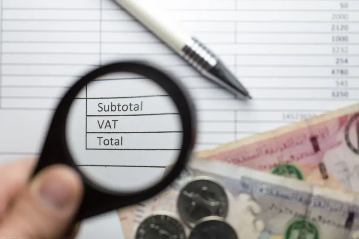 Pod lupą widać napisy "Subtotal", "VAT", "Total" na tle dokumentu z cyframi. Obok leżą banknoty i monety, co sugeruje analizę finansową zgodną z art. 96 ust. 9a pkt 2.