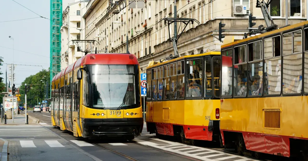 Dwa żółto-czerwone tramwaje stoją na ulicy, jeden z nich ma pierwszeństwo.