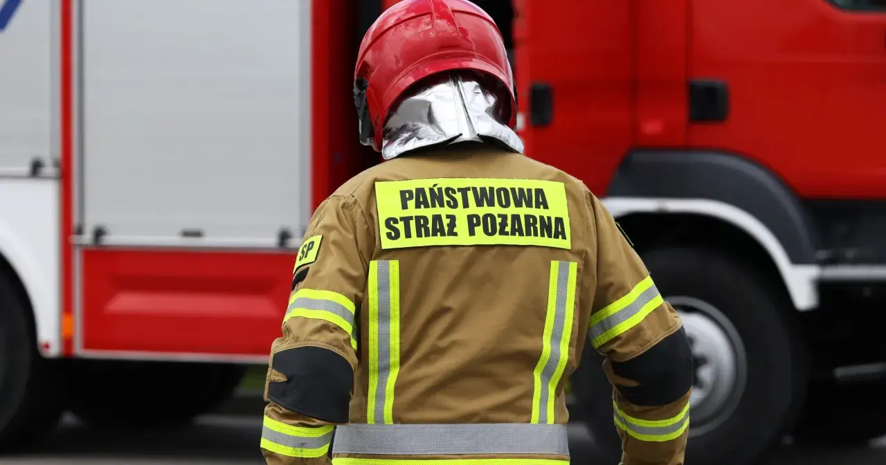 Strażak w hełmie i kurtce z napisem "Państwowa Straż Pożarna" gotowy do akcji. Alarm bombowy? Nie, to tylko ćwiczenia.