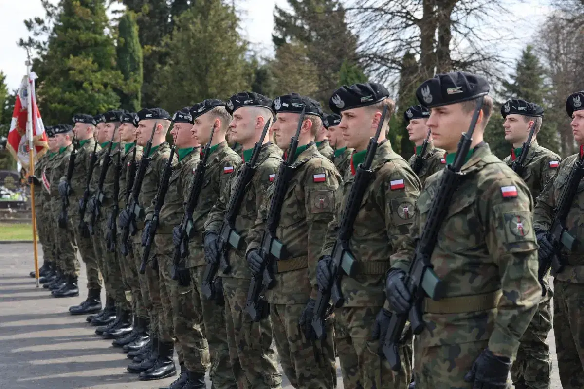 Kombatanci w mundurach i beretach stoją w szeregu, trzymając broń.