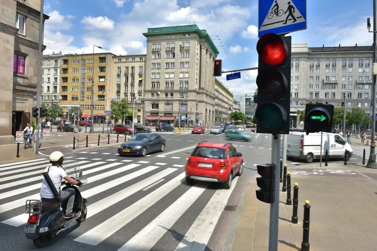 Sygnalizator S2 z czerwonym światłem dla samochodów i zieloną strzałką dla kierunku jazdy. Na pasach skuter i samochody.