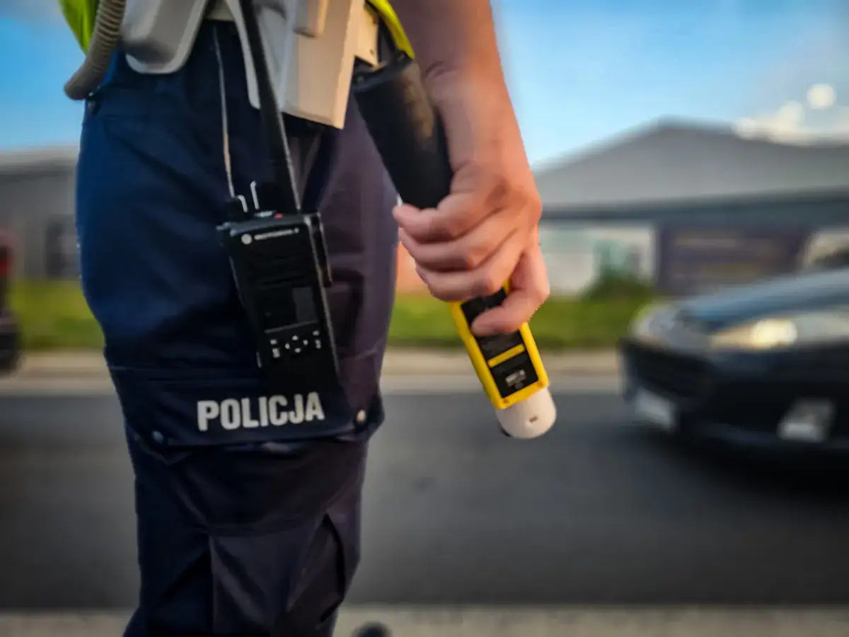 Policjant z alkomatem w ręku, gotowy do kontroli trzeźwości zgodnie z 178a kk. Obok radiostacja Motorola.