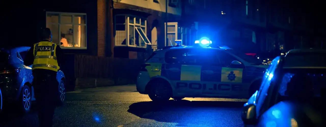 Nocna interwencja policji. Radiowóz z włączonymi sygnałami świetlnymi stoi przed domem. To obraz, który może symbolizować egzekwowanie prawa, w tym ustawy antyprzemocowej.