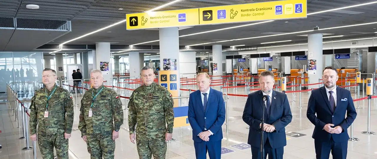 Pięciu mężczyzn, trzech w mundurach wojskowych, stoi przed stanowiskami kontroli granicznej.
