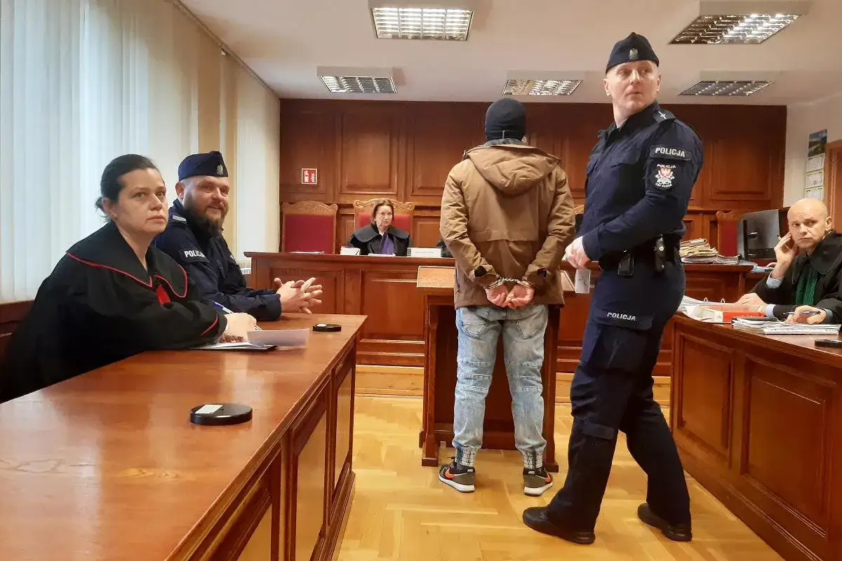 Sąd rozpatruje sprawę z art. 233 kk. Aresztowany mężczyzna stoi przed sędzią i policjantem.