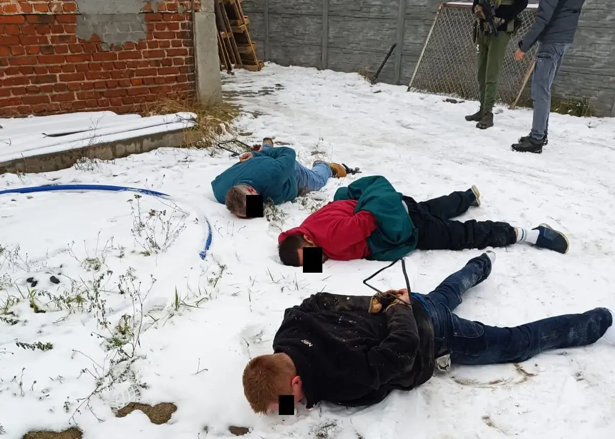 Trzech mężczyzn leży na śniegu, ręce skrępowane. Policja zatrzymała ich w związku z produkcją metamfetaminy.