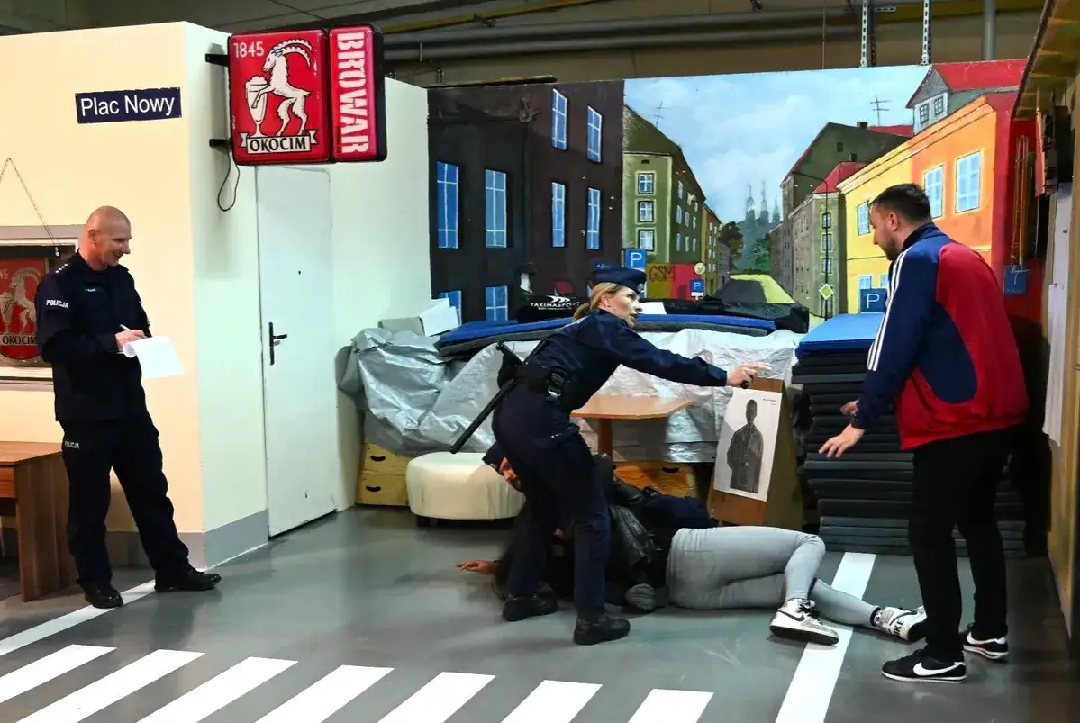 Ćwiczenia w szkółkach policyjnych: policjantka obezwładnia zatrzymanego, podczas gdy kolega obserwuje.