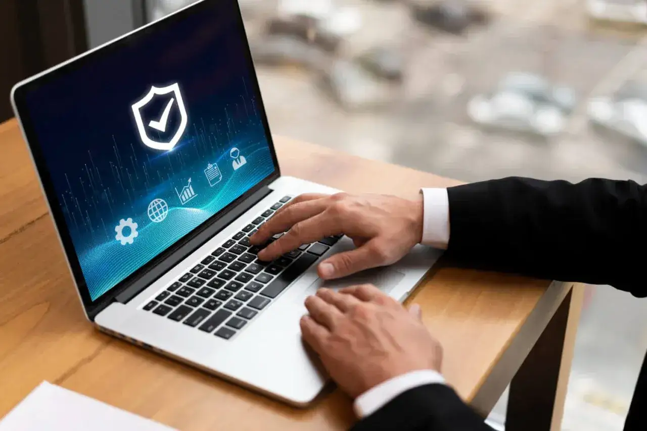 Ręce na klawiaturze laptopa, na ekranie tarcza z zaznaczeniem, symbolizująca bezpieczeństwo. Czy to próba zapobieżenia sabotażowi?