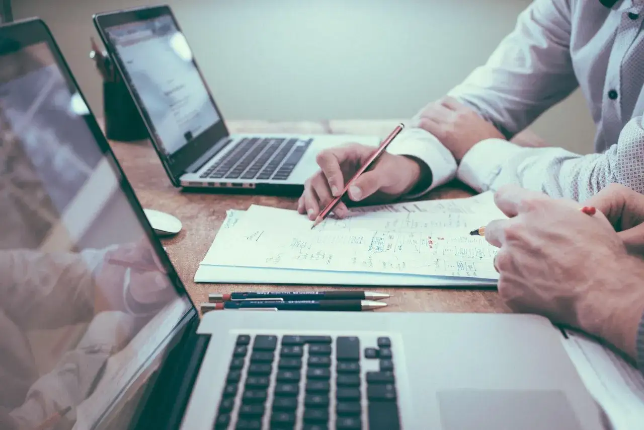 Dwie osoby analizują dokumenty przy laptopach. Pracują nad strategią, która może być powiązana z funduszem gwarantowanych świadczeń pracowniczych.