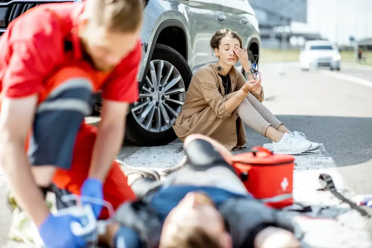 Ratownik udziela pomocy poszkodowanemu po wypadku. Kobieta siedzi obok, wyraźnie wstrząśnięta. To nie była ucieczka z miejsca kolizji, lecz dramatyczna akcja ratunkowa.