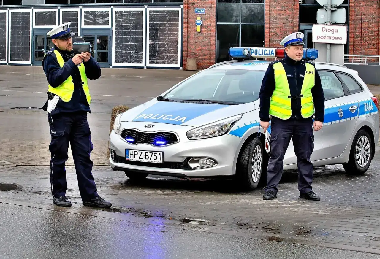 Policjanci z radarem mierzą prędkość. Jeden celuje, drugi stoi obok radiowozu. Uważaj na przekroczenie prędkości o 30 km/h!