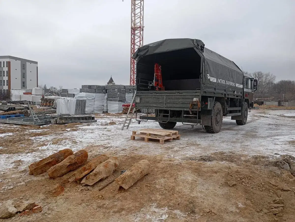 Na placu budowy leżą cztery zardzewiałe niewybuchy. Obok stoi wojskowa ciężarówka z napisem 