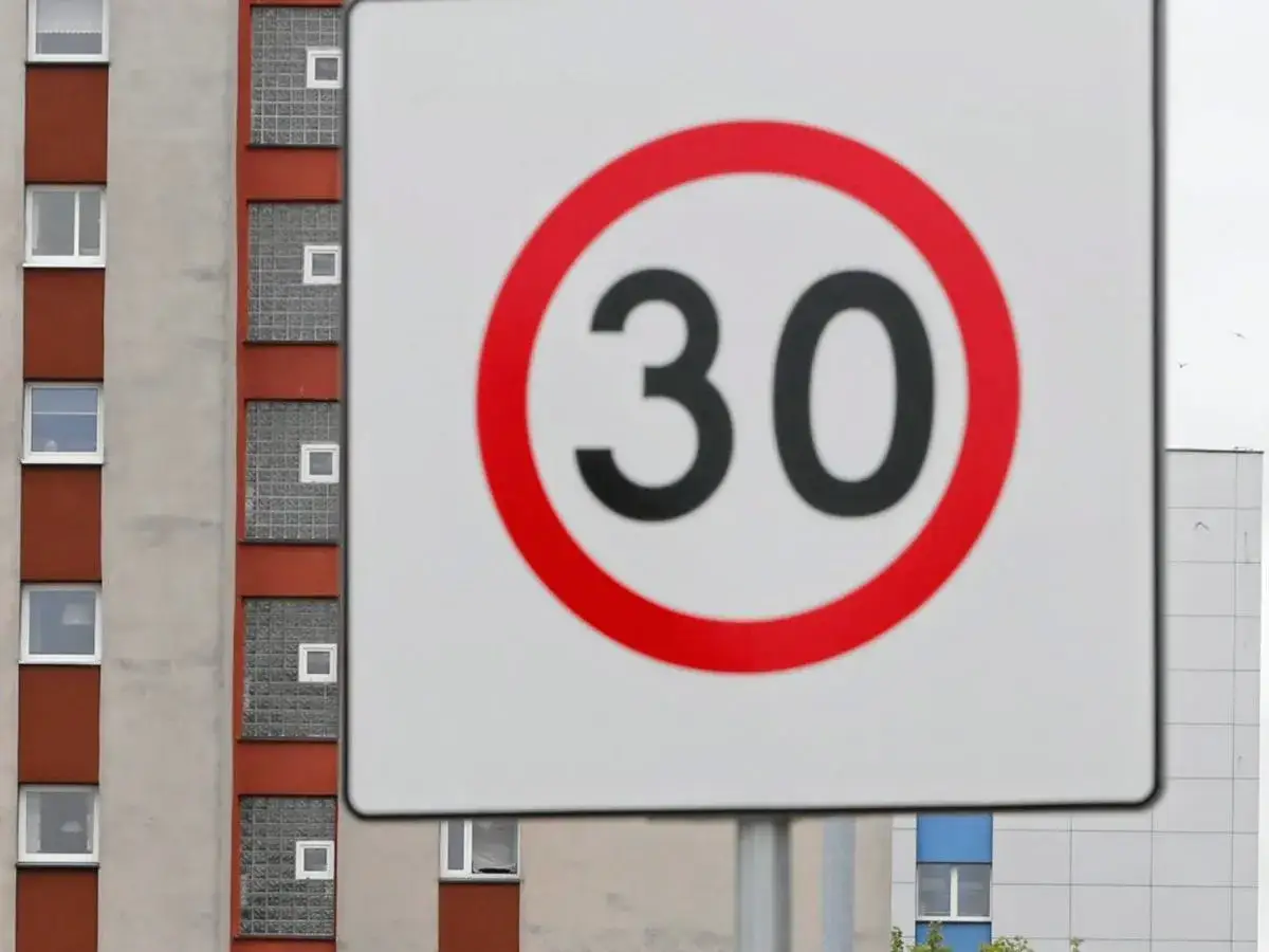Znak d43 informuje o ograniczeniu prędkości do 30 km/h. W tle widać fragmenty budynków mieszkalnych.