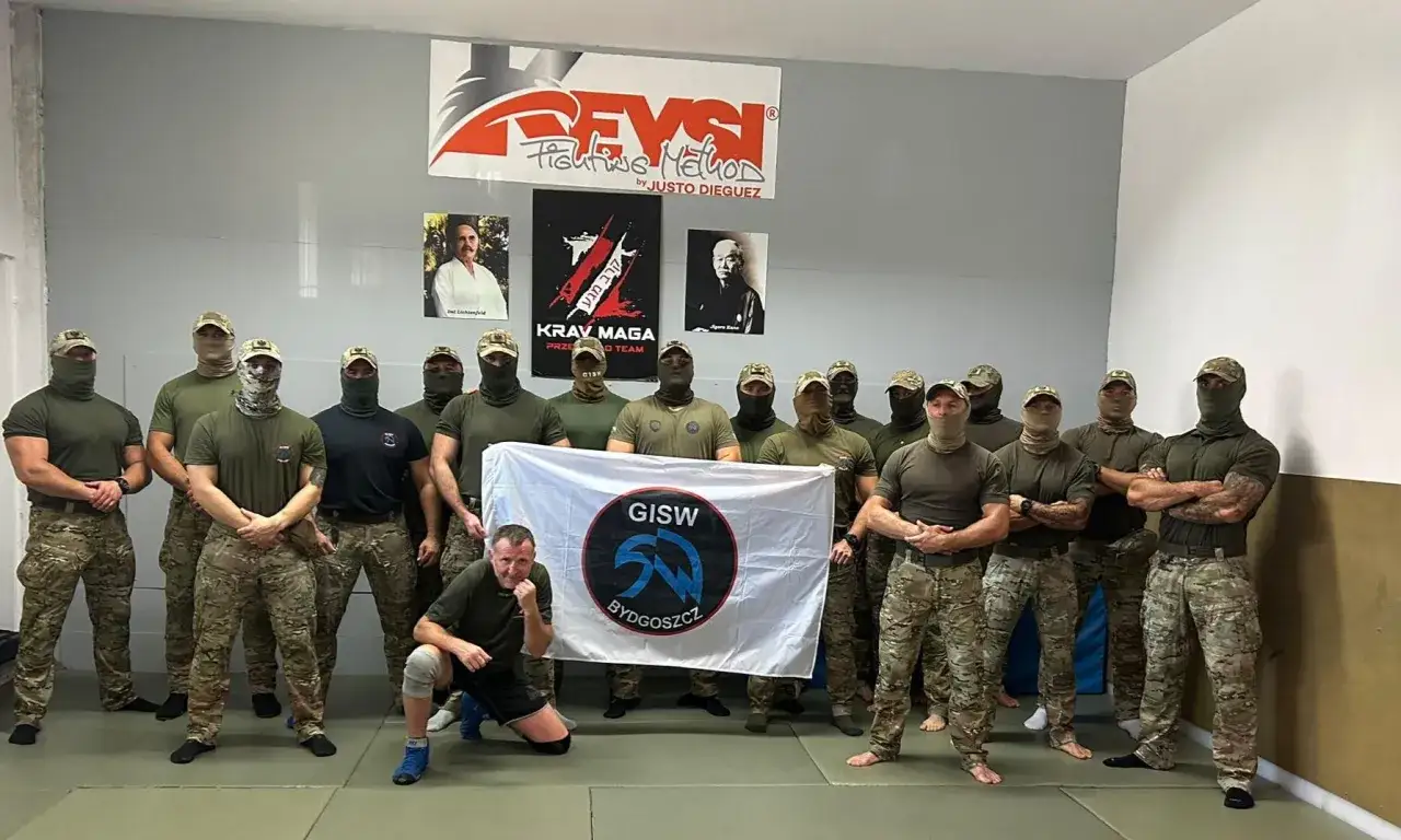 Grupa mężczyzn w mundurach i kominiarkach pozuje z flagą GISW Bydgoszcz.