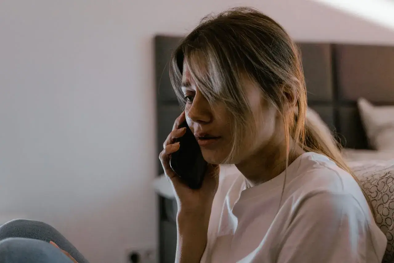 Zmartwiona kobieta odbiera telefon, słysząc groźby szantażu. Jej twarz wyraża niepokój i strach.