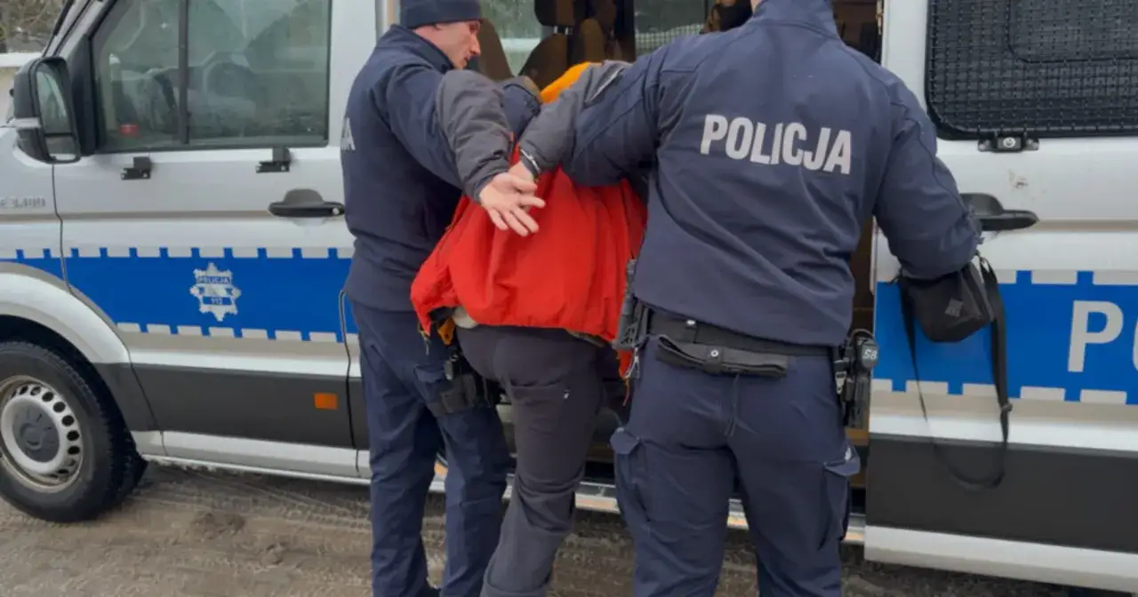 Policjanci eskortują zatrzymanego do radiowozu. Sprawa dotyczy wyłudzenia haraczu.