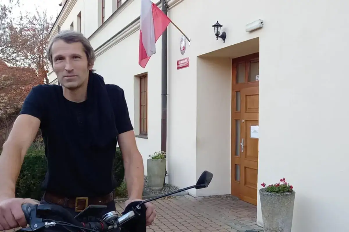 Mężczyzna na rowerze przed budynkiem z polską flagą. Czy to precedens, że tak łatwo tu dotarł?