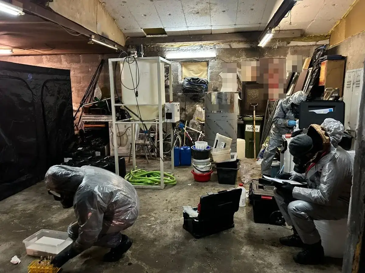 Funkcjonariusze w kombinezonach zabezpieczają laboratorium, gdzie produkowano amfetaminę. Widać sprzęt chemiczny i pojemniki.
