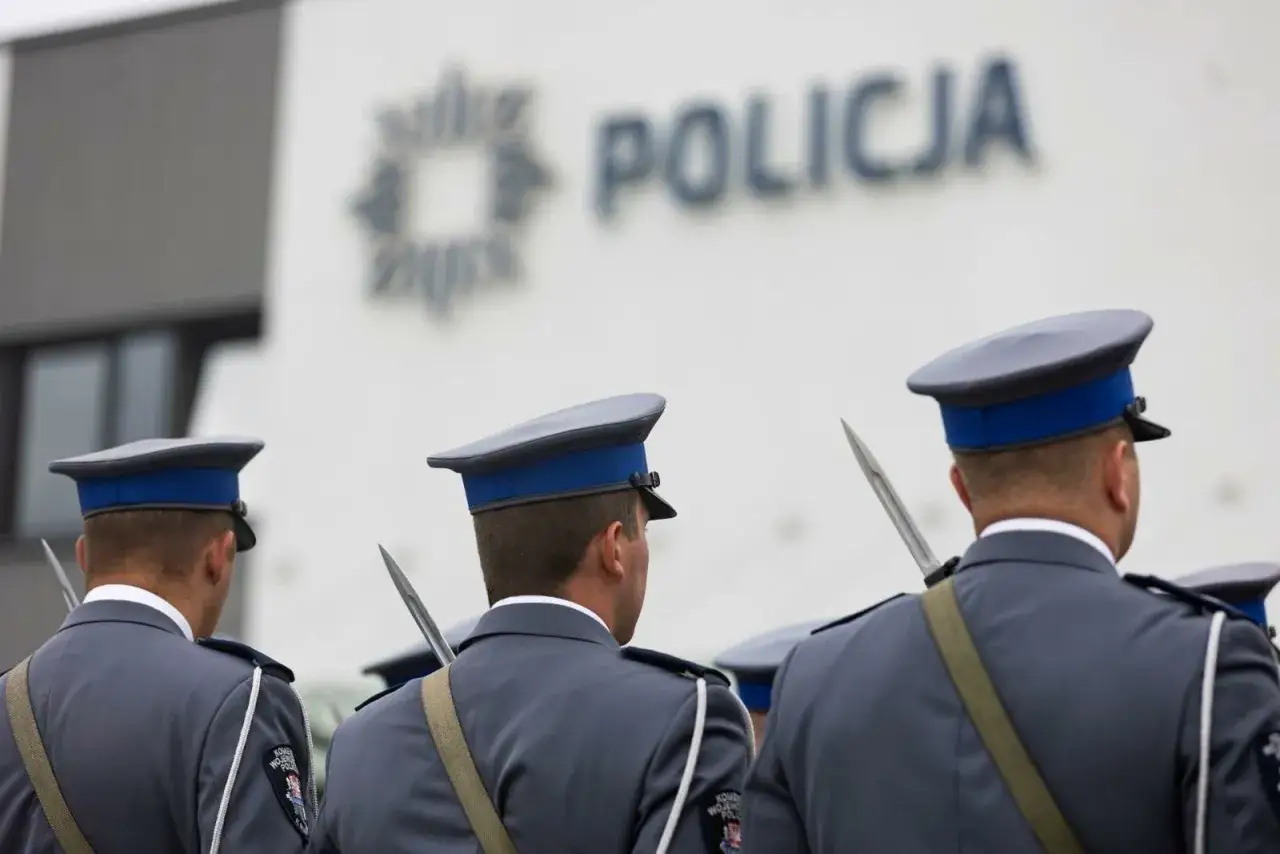Policjanci w mundurach, z bagnetami przy pasach, czekają na mianowanie na nowych zasadach przed budynkiem policji.