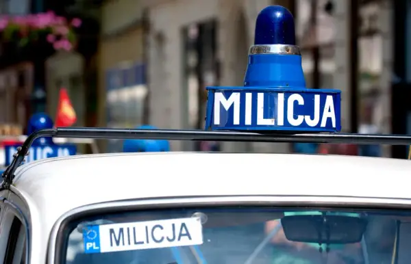 Niebieska lampa i napis "MILICJA" na dachu białego samochodu.